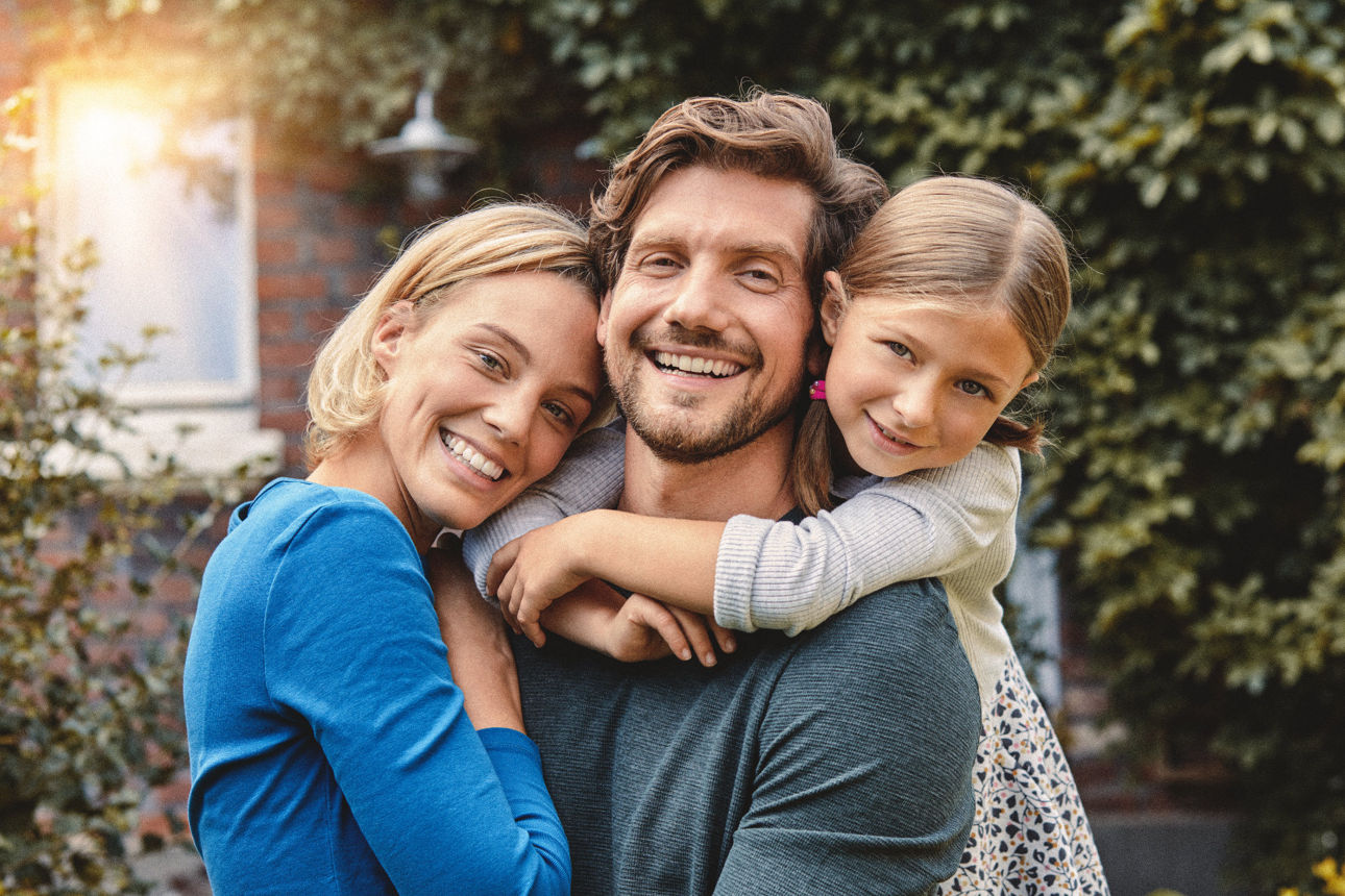 Glückliche Familie mit Vater, Mutter und Tochter umarmt sich im Garten.