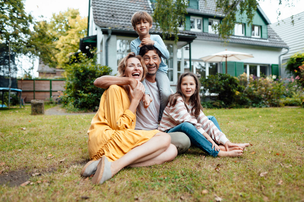 Familie sitzt im Garten vor einem Haus