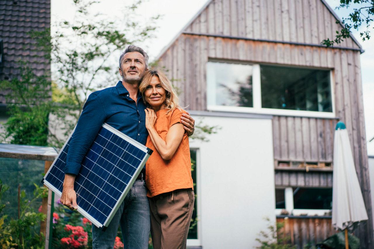 Pärchen steht vor Haus und der Mann hat ein Solarpanel in der Hand