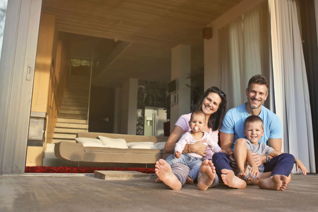 Junge Familie mit zwei Kindern sitzt auf der Veranda ihres Neubaus.