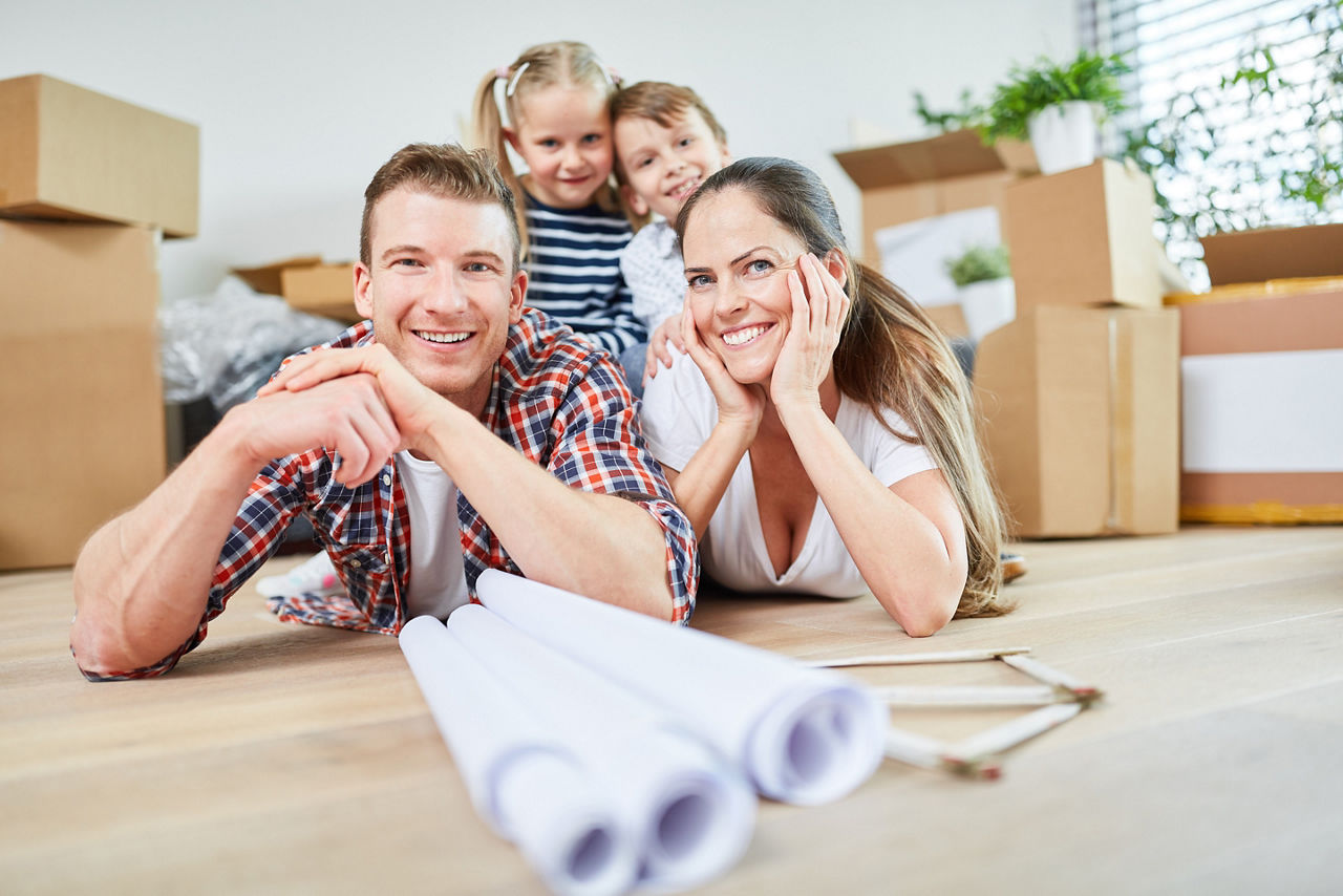 Eine glückliche Familie liegt zwischen Umzugskartons auf dem Boden und plant ihr neues Zuhause.