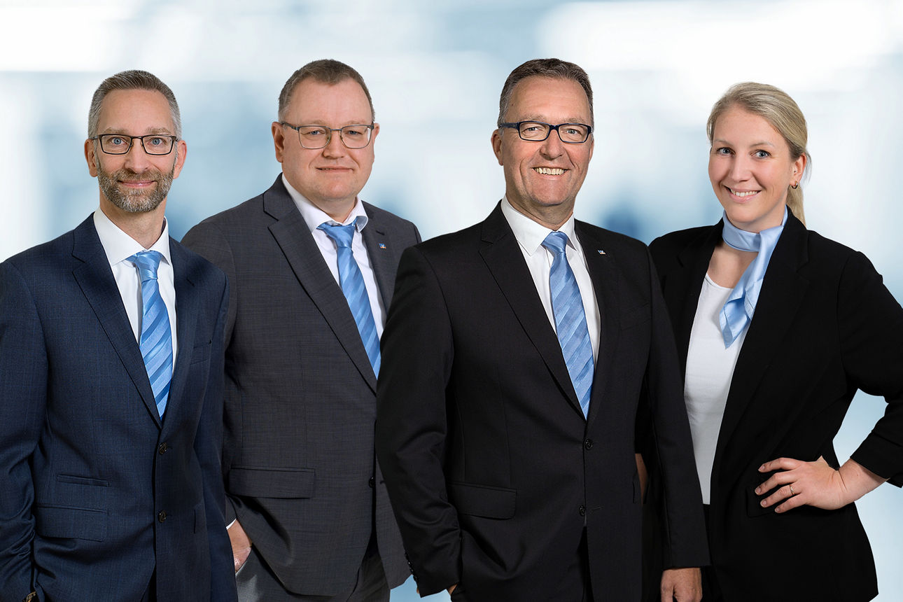 drei Männer und eine Frau in schwarzen Anzügen