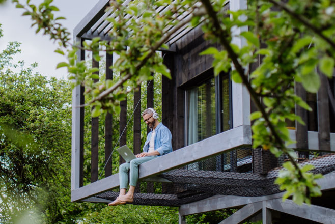 Mann sitzt mit Laptop und Kopfhörern auf dem Vorsprung seines Hauses.
