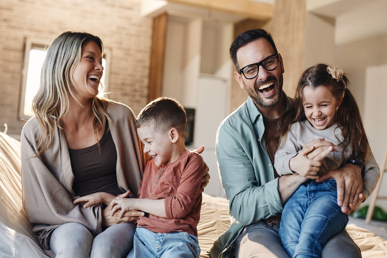 Eine vierköpfige Familie sitzt fröhlich lachend auf dem Sofa