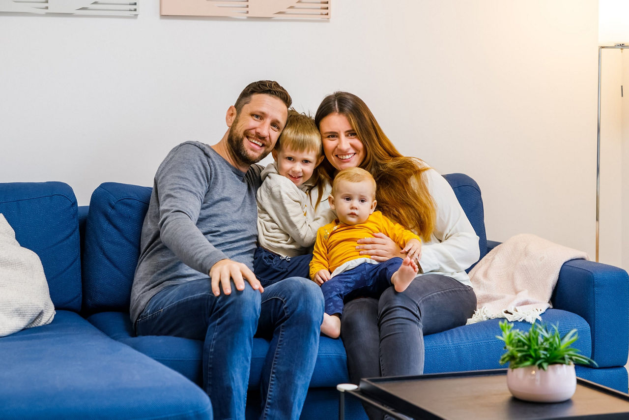 junges glückliches Paar sitzt mit zwei Kindern auf einem Sofa und lacht in die Kamera