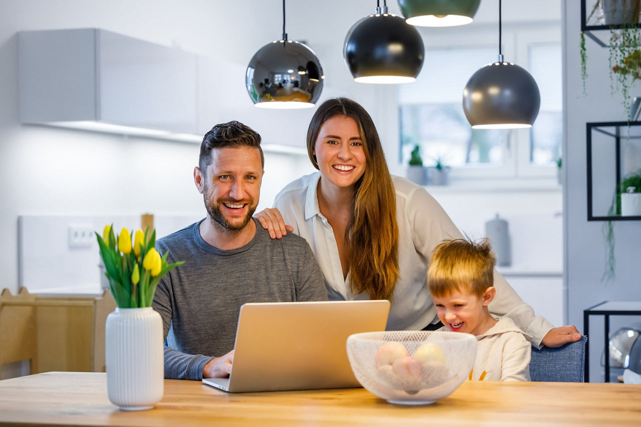 Glückliches junges Paar sitzt mit Kind vor einem Laptop