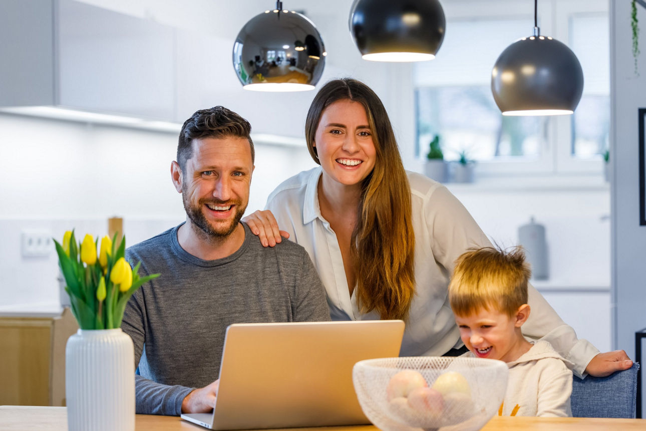 Glückliches junges Paar sitzt mit Sohn vor einem Laptop