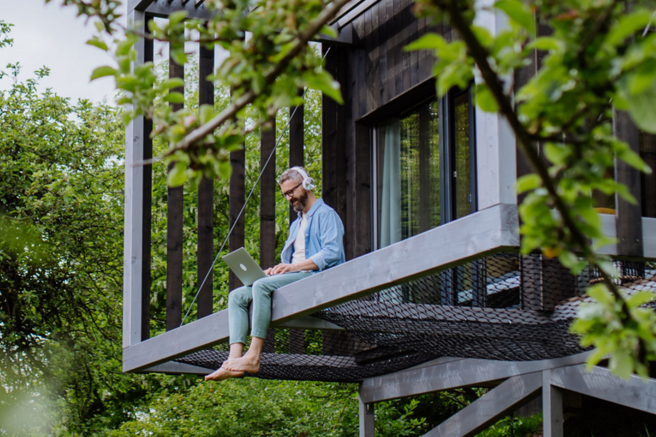 Mann mit Laptop sitzt auf einem Hausvorsprung