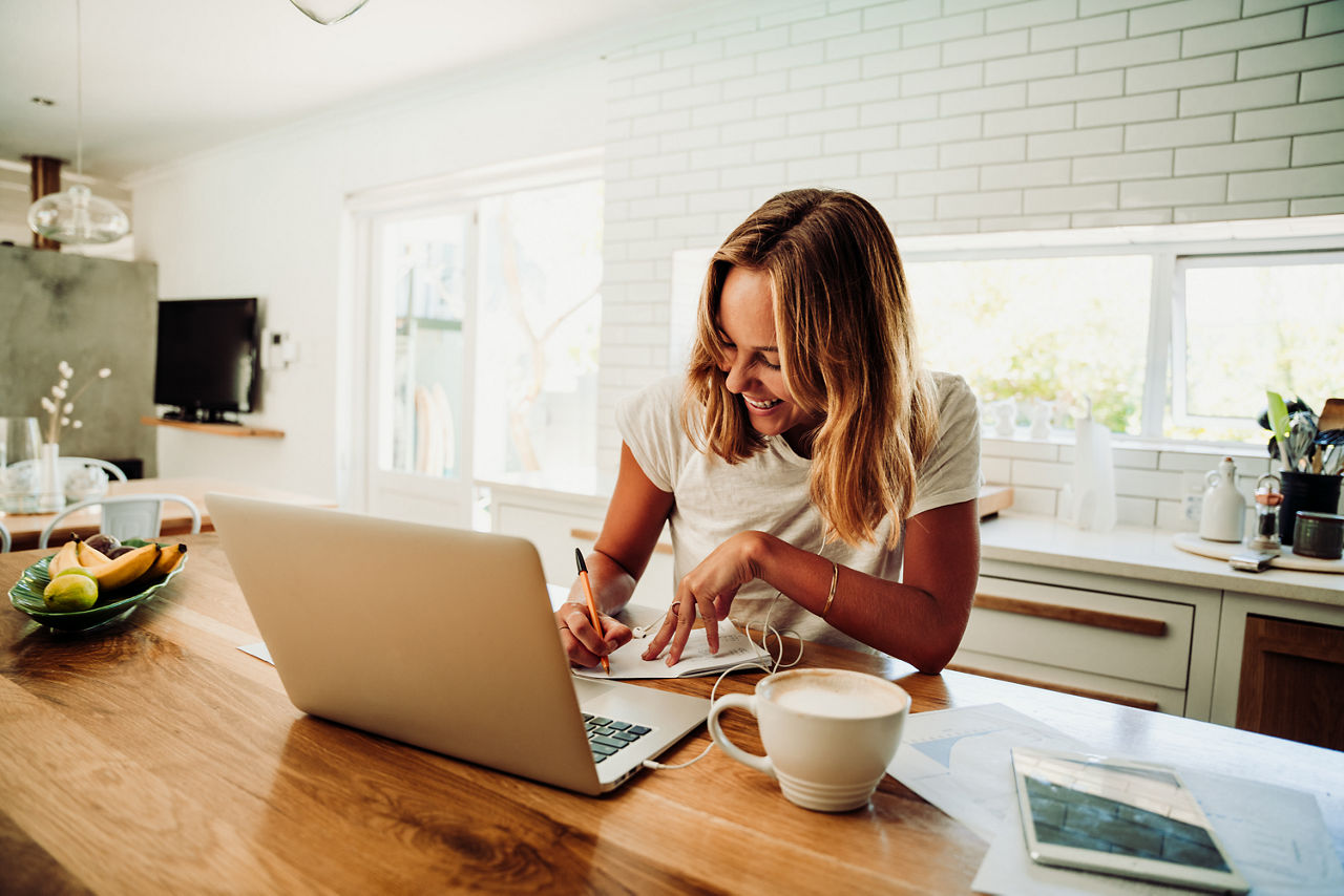 Eine Frau sitzt am mit Laptop und Kaffee am Tisch und arbeitet