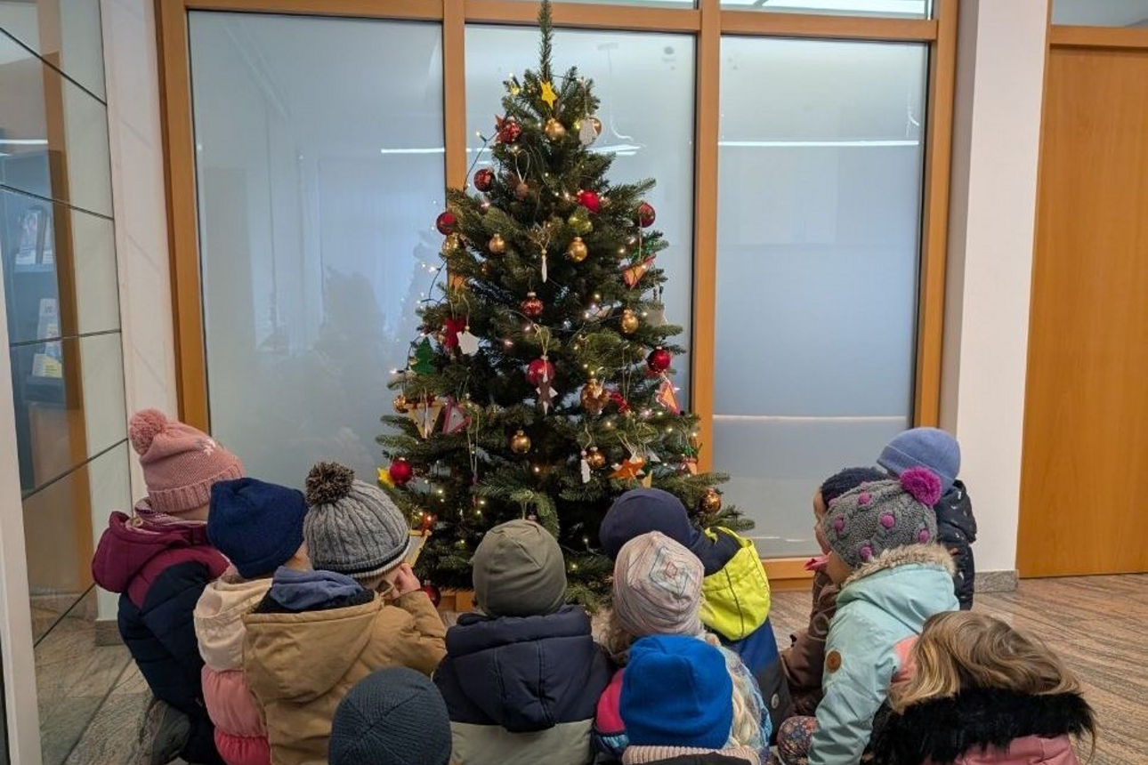 Kinder sitzen um den von ihnen geschmückten Weihnachtsbaum in der Filiale