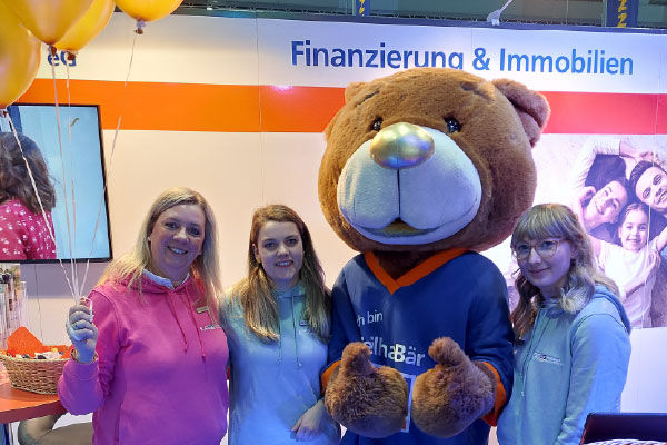 3 Mitarbeiterinnen stehen zusammen mit dem Maskottchen dem TeilhaBär am Veranstaltungsort
