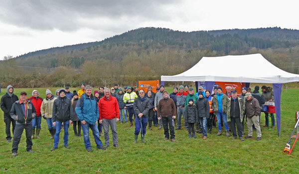 Viele Personen, Kinder und Erwachsene, stehen auf einer grünen Wiese mit einem Pavillon. Sie befinden sich gerade beim Schnittkurs. 