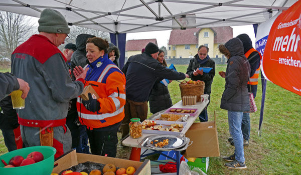Mehrere Menschen stehen unter einem Pavillon-Zelt und bedinene sich an einem aufgestellten Buffet.