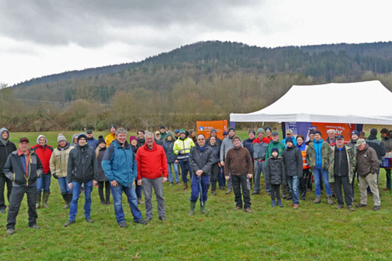Viele Personen, Kinder und Erwachsene, stehen auf einer grünen Wiese mit einem Pavillon. Sie befinden sich gerade beim Schnittkurs. 