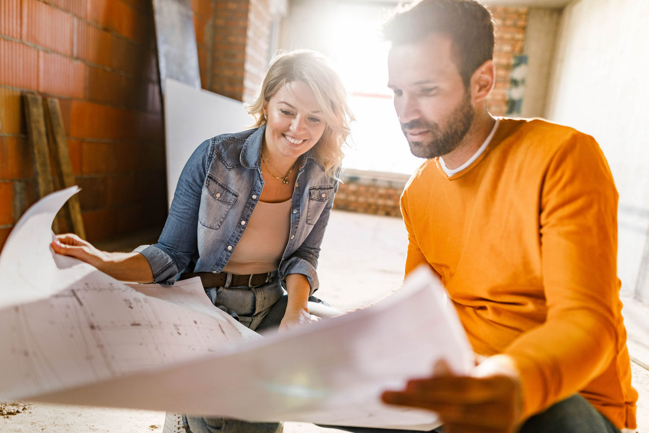 Young happy couple examining blueprints during home renovation process in the apartment. Focus is on woman.