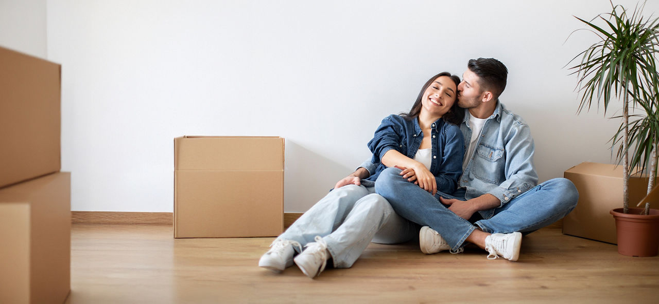 Junges Paar sitzt neben Kartons in einer neuen Wohnung
