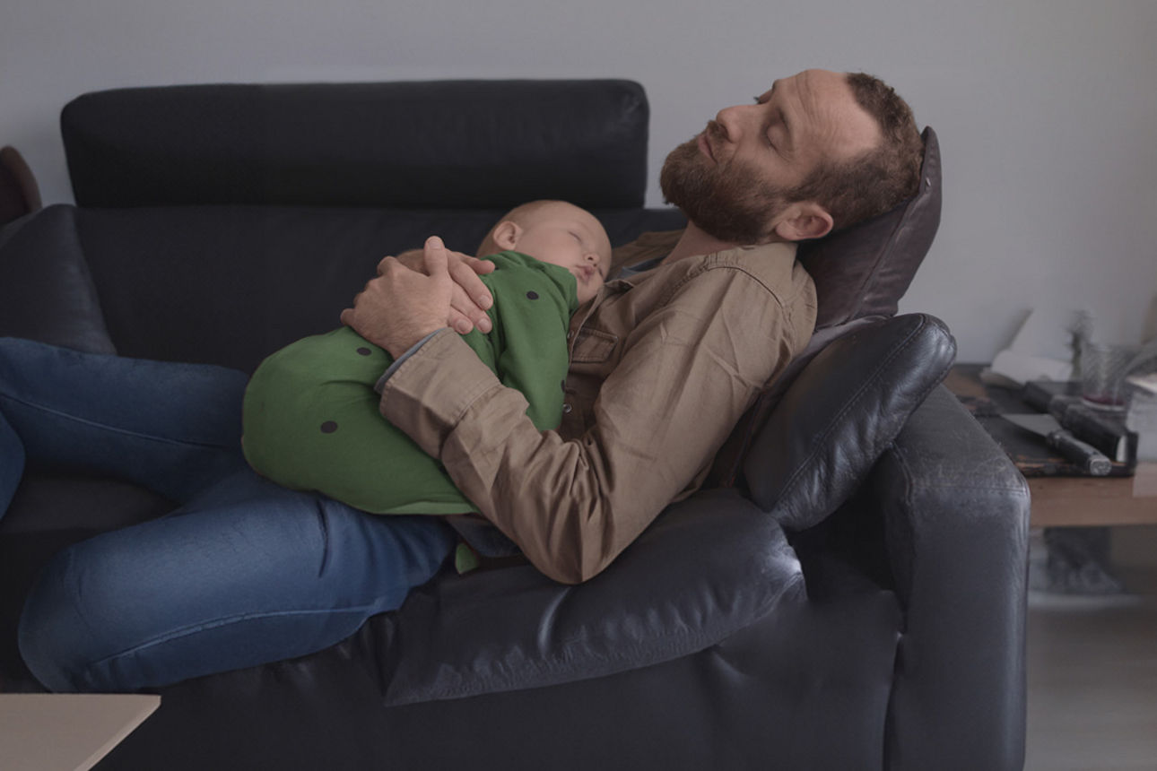 Vater liegt mit einem Baby auf einer Couch.