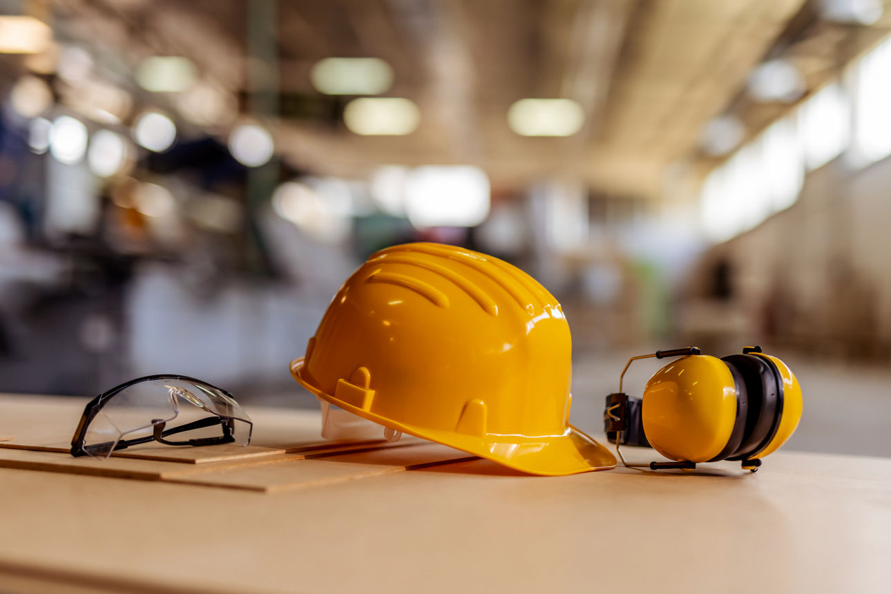 Schutzhelm, Gehörschutz und Brille auf Werkbank in industrieller Umgebung.