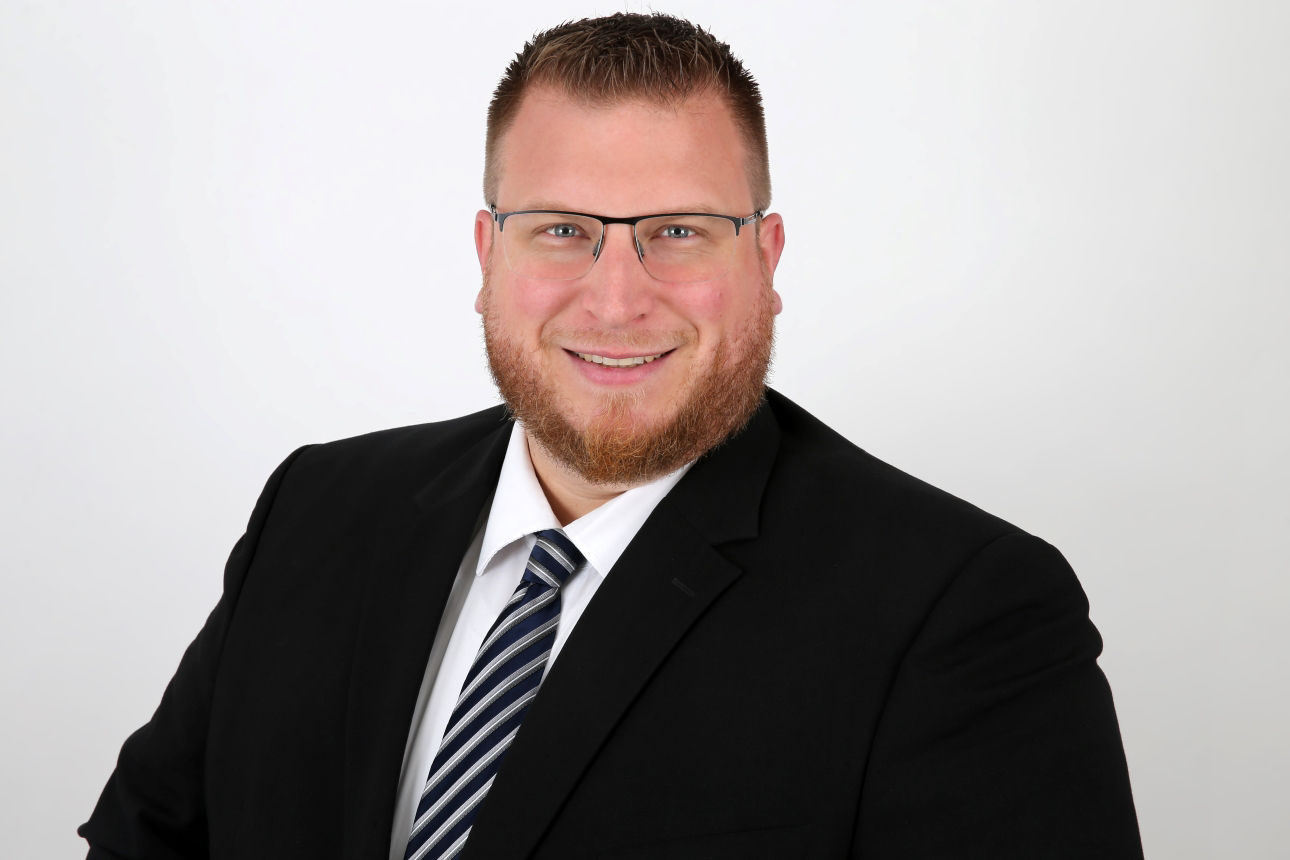 Ein lächelnder Mann in einem Anzug schaut in die Kamera.