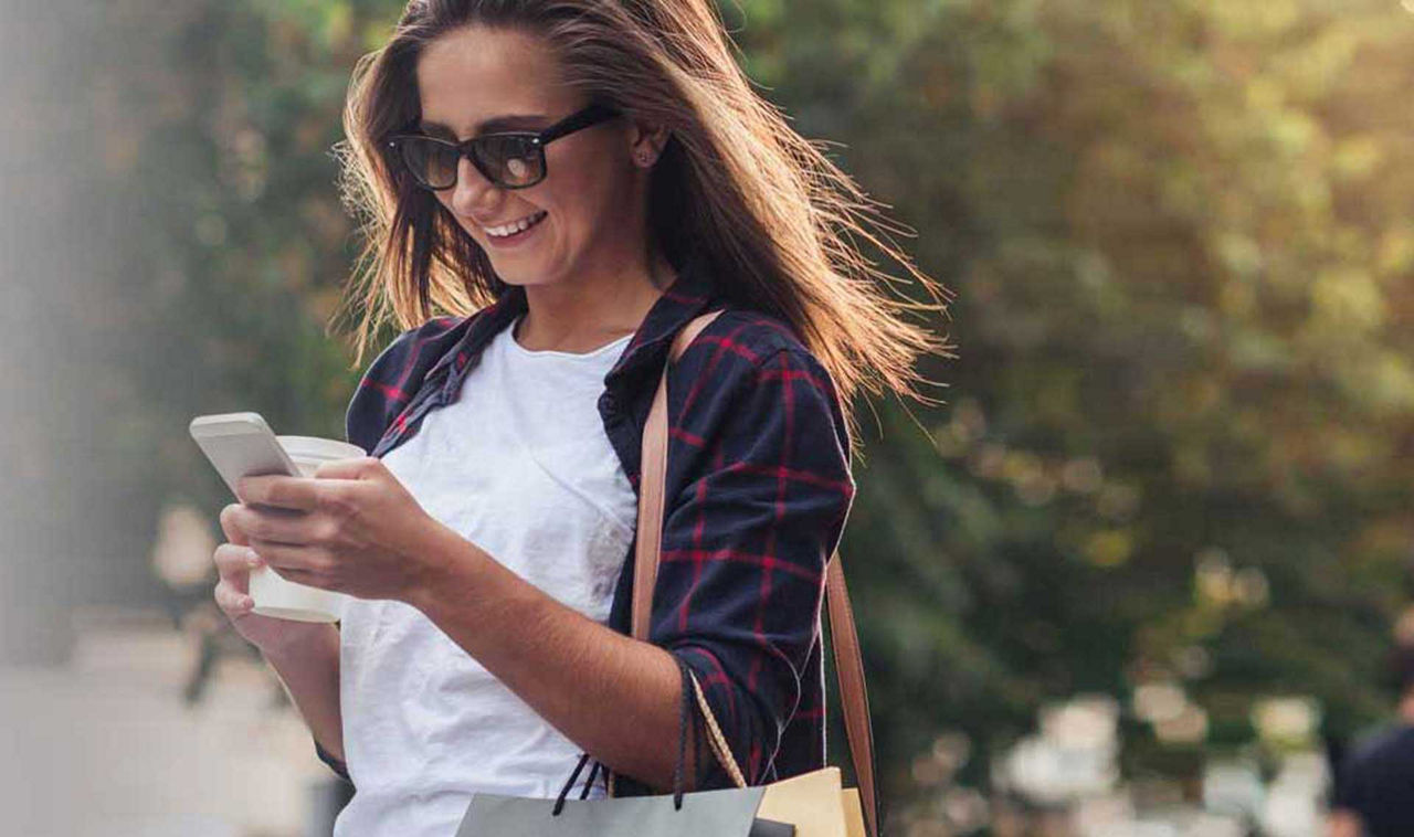 Service-Hotline - Frau mit spaziert mit Kaffe und Handy in der Hand