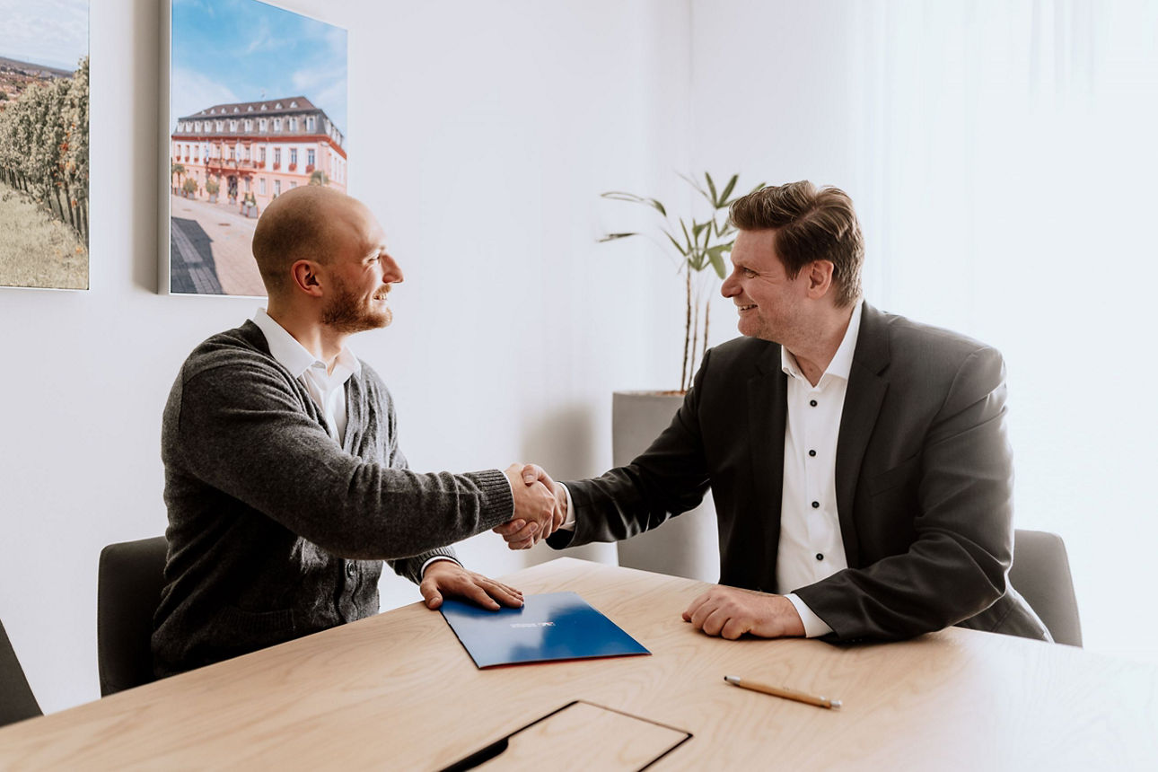 Zwei Männer am Besprechungstisch geben sich die Hand.