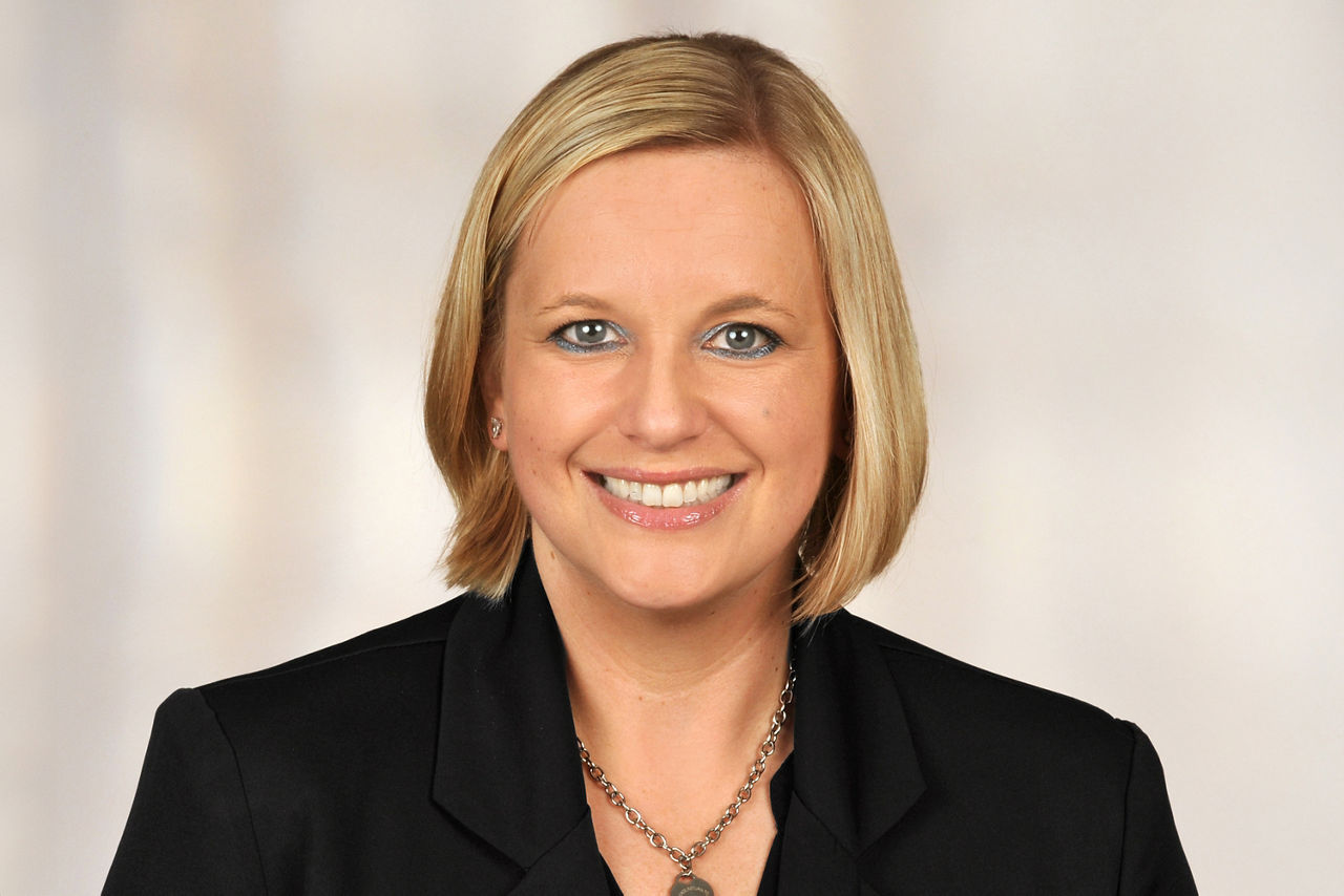 Frau mit schulterlangem blondem Haar trägt schwarzen Blazer und silberne Kette mit Anhänger