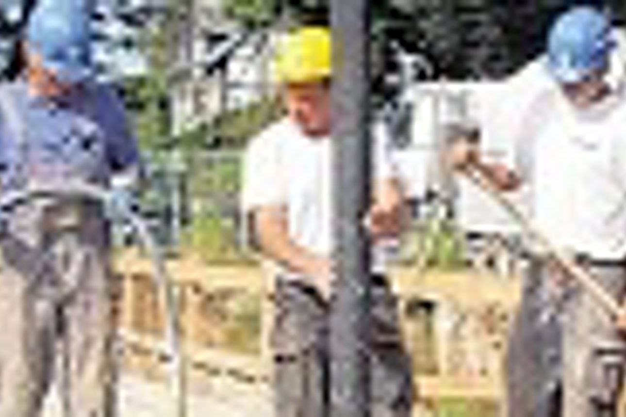 Drei Männer in Arbeitskleidung und mit Schutzhelmen gießen Zement auf eine Plattform