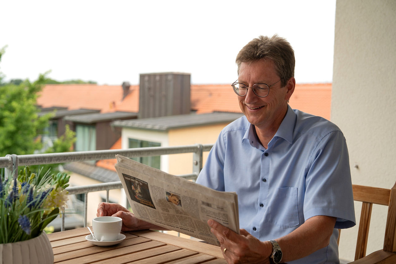 Mann sitzt auf dem Balkon und liest Zeitung