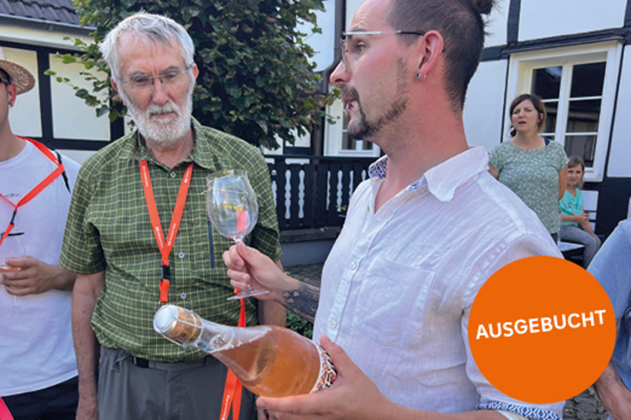 Mehrere Personen, wovon ein Mann ein Weinglas und eine Flasche Wein in der Hand hält