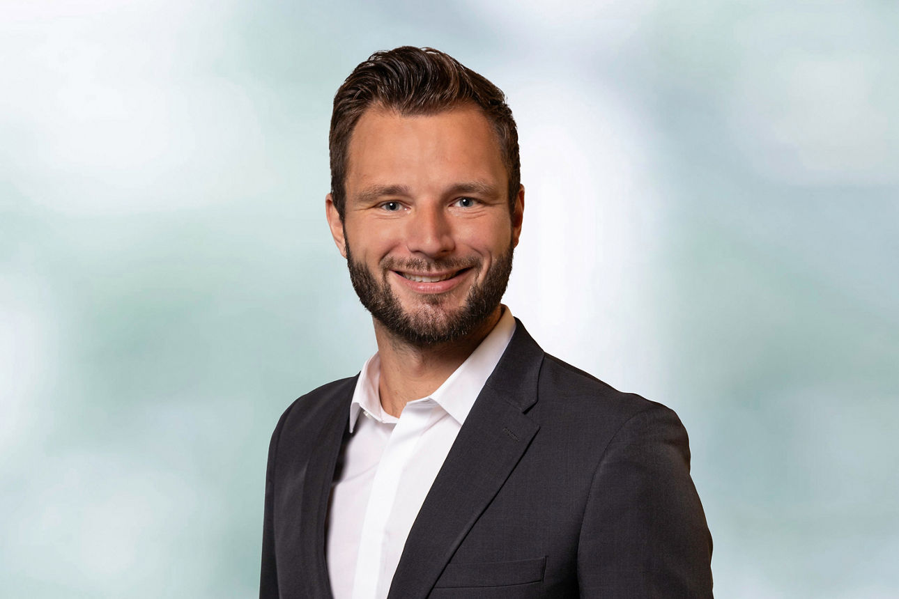 Portrait unseres Mitarbeiters Florian Berner. Weißes Hemd, Graues Sakko, freundlich lächender Mann mit Bart.