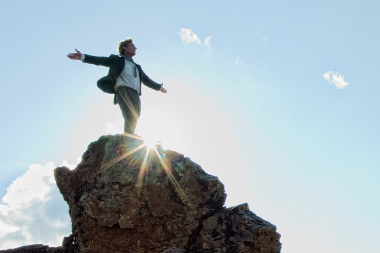 Ein Bergsteiger auf einem Gipfel breitet die Arbei aus