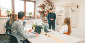 Eine Gruppe Mitarbeiter sind in einer Schulung und diskutieren um ein Whiteboard herum