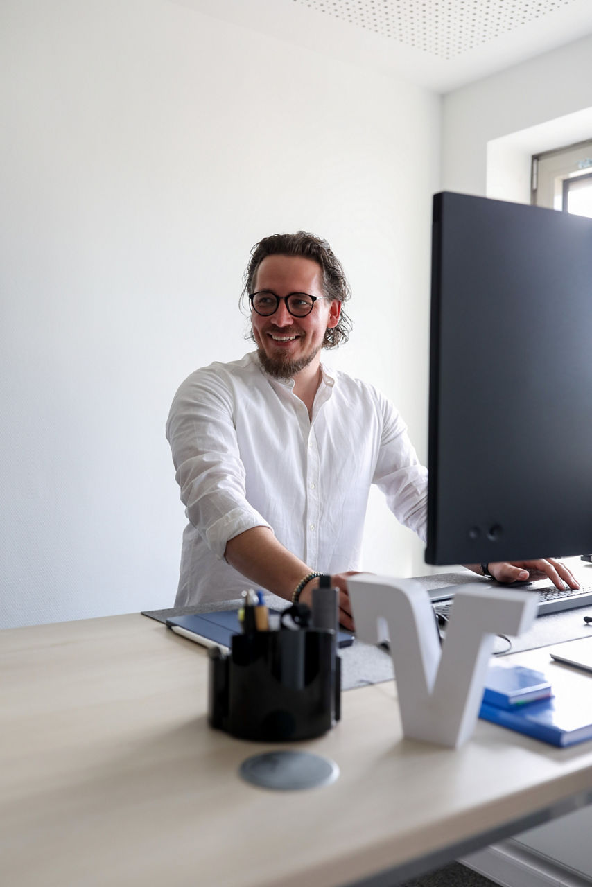 Eine lächelnder Mann steht an seinem Arbeitsplatz