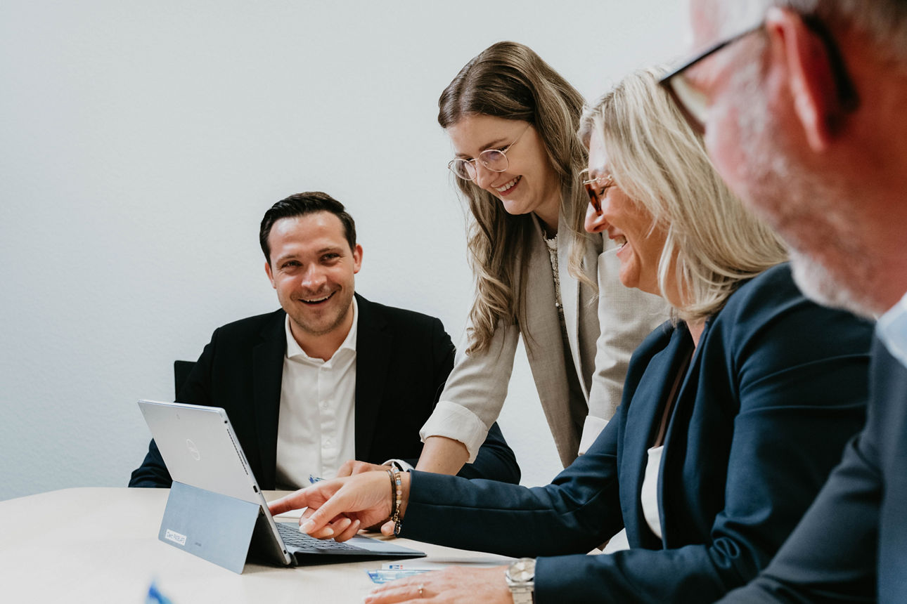Junge Frau und junger Mann im Gespräch an einem Besprechungstisch mit Unterlagen, Stiften und Wasserflasche.