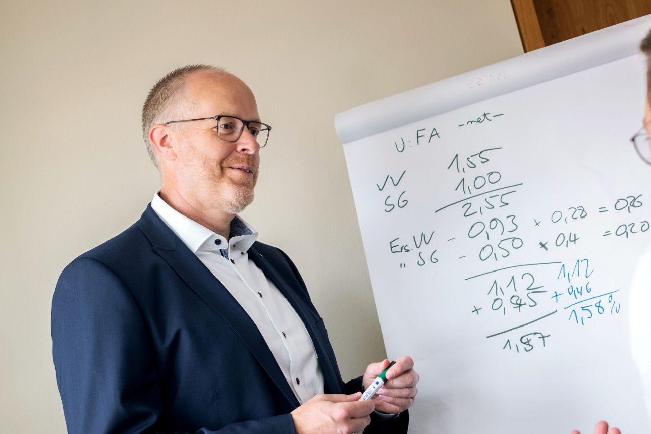 Ein Bankmitarbeiter steht vor einem Whiteboard und redet mit einem Kollegen