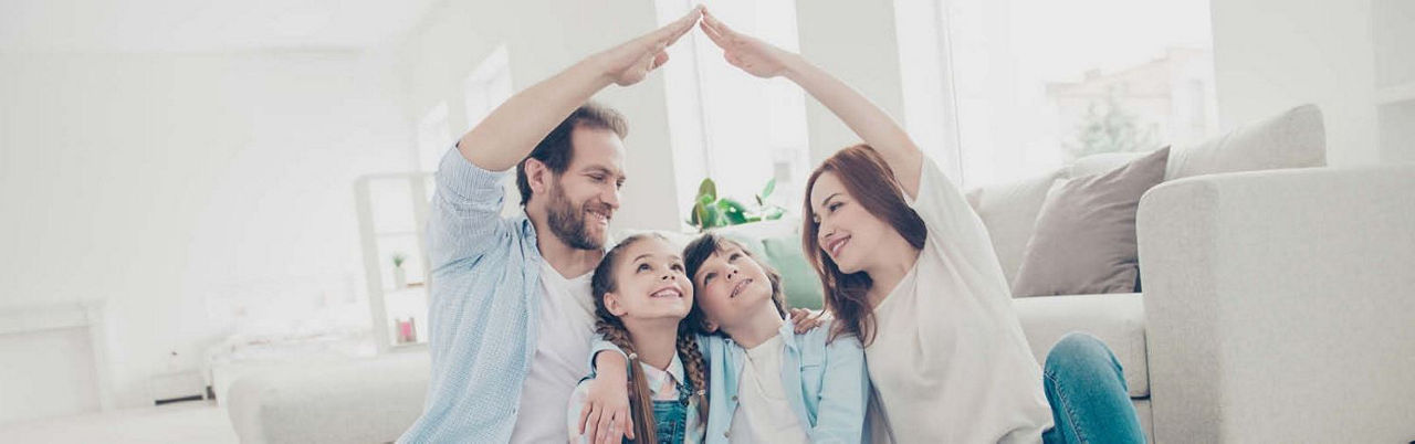 Eine Familie sitzt vor dem Sofa, bildet mit den Händen ein Dach über die Kinder