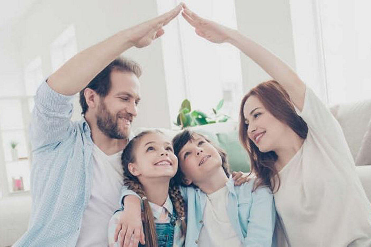 Eine Familie sitzt vor dem Sofa, bildet mit den Händen ein Dach über die Kinder