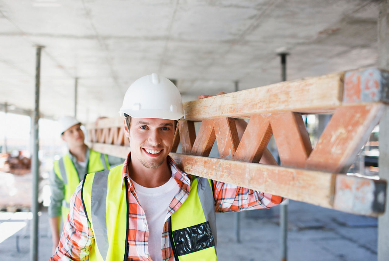 Zwei Bauarbeiter, die auf einer Baustelle ein Holzelement tragen