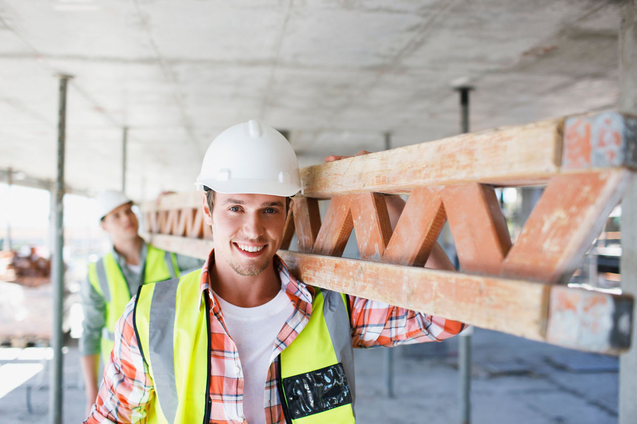 Zwei Bauarbeiter, die auf einer Baustelle ein Holzelement tragen