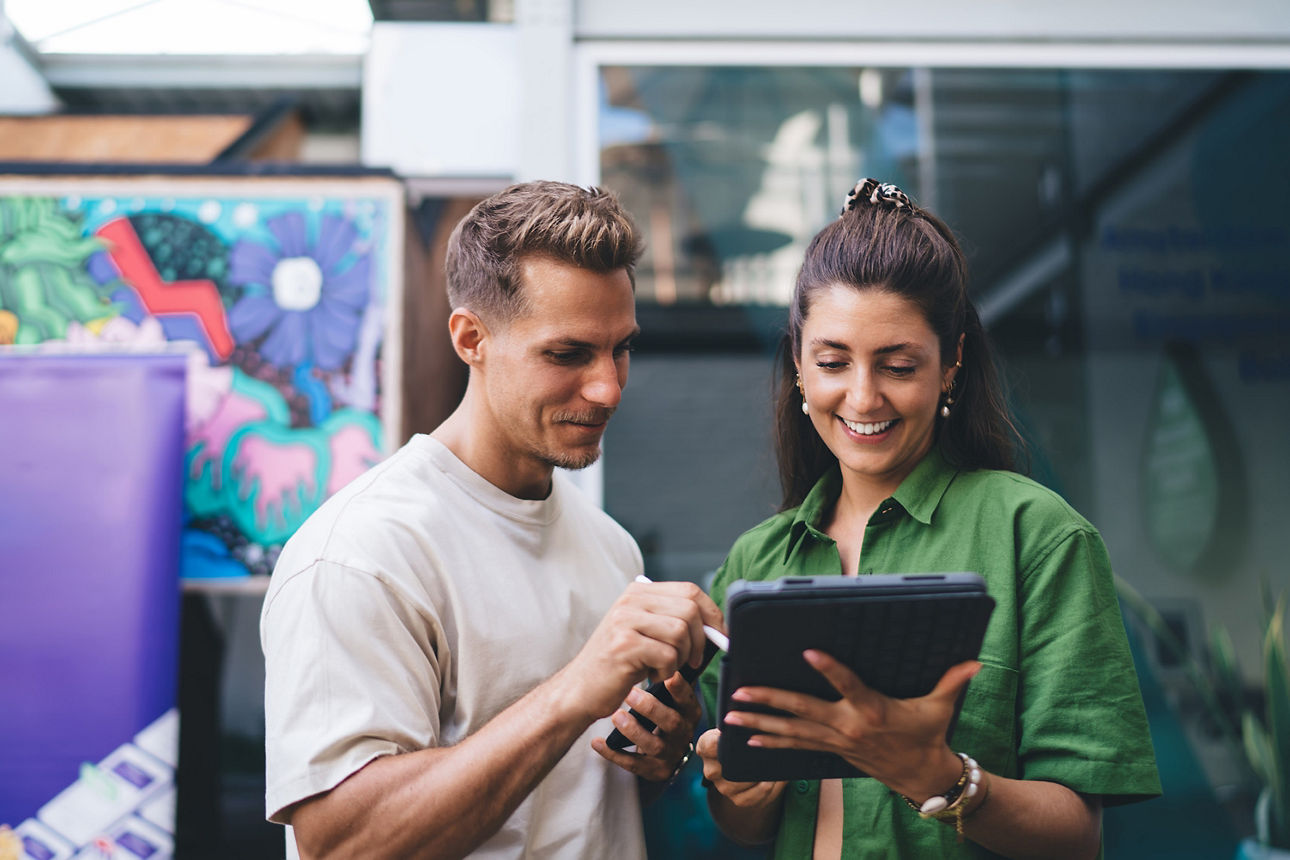 Eine Frau und ein Mann schauen auf ein Tablet und lächeln.