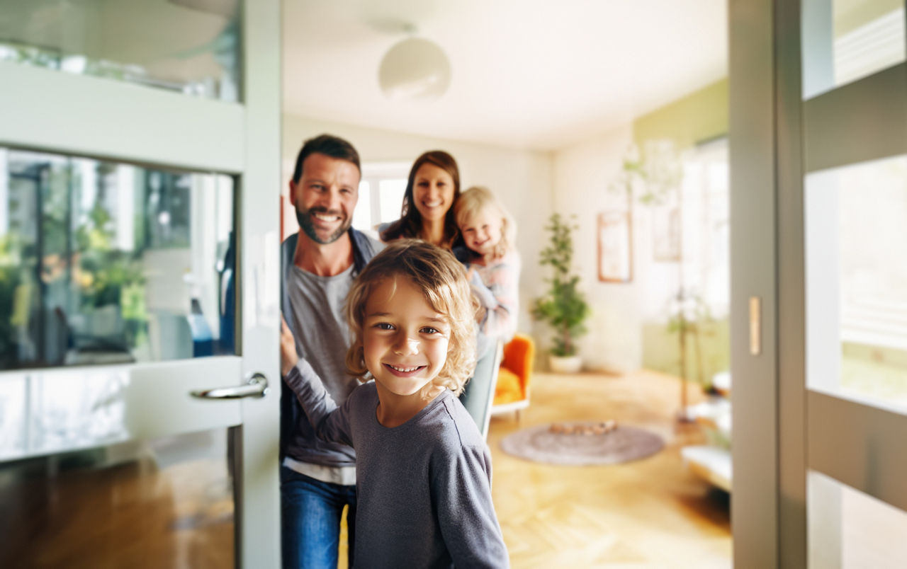 Eine freundliche Familie begrüßt die Gäste vor der Tür ihres neuen Zuhauses. Ein kleiner Junge hält die Tür auf und lächelt i