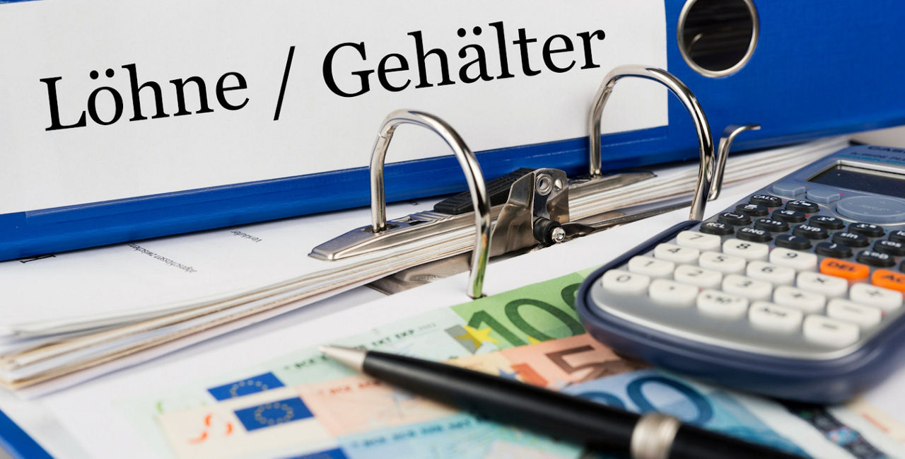 Ein Ordner Löhne / Gehälter liegt mit einem Taschenrechner, einem Stift und ein paar Geldscheinen auf einem Tisch