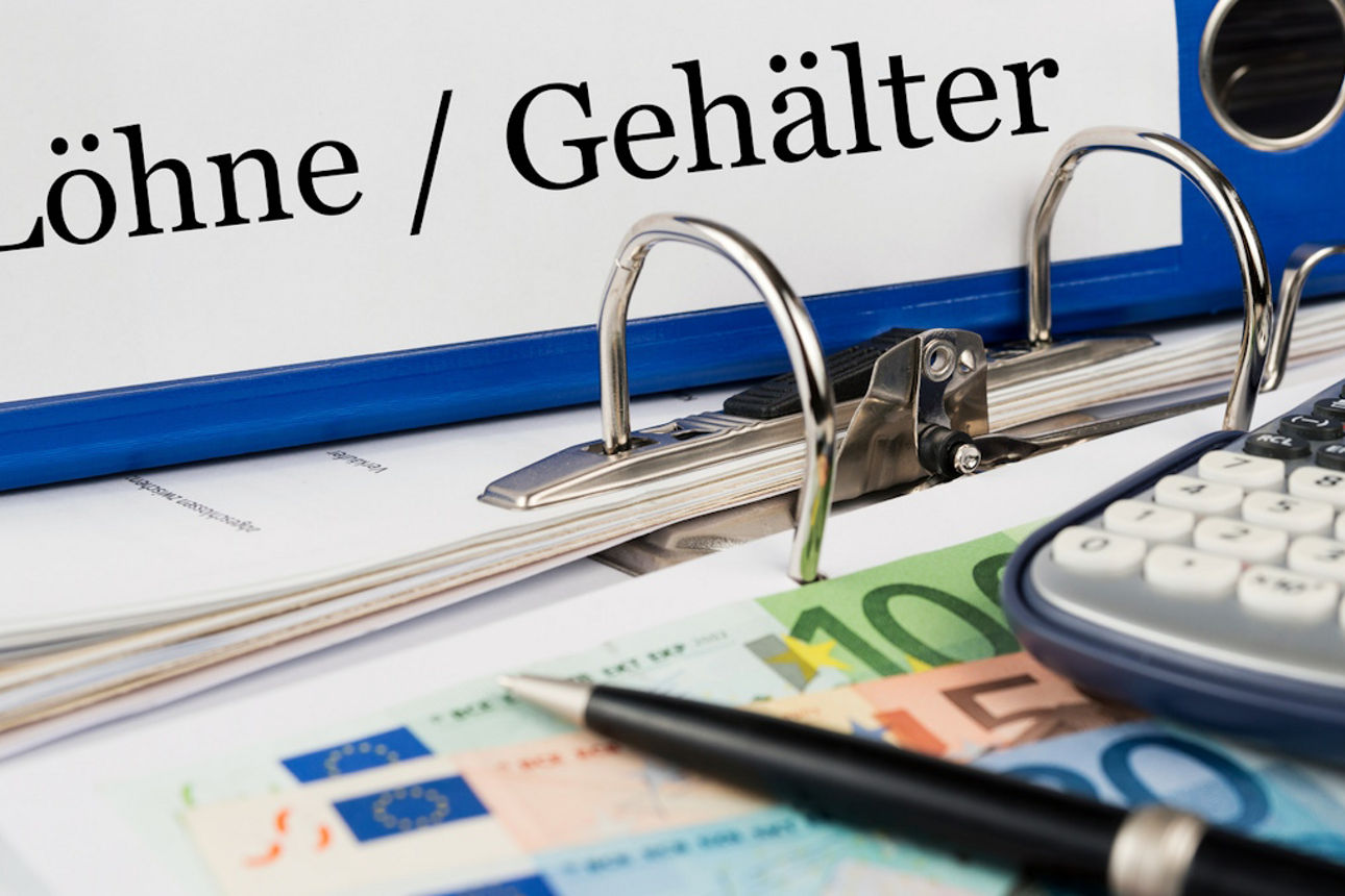 Ein Ordner Löhne / Gehälter liegt mit einem Taschenrechner, einem Stift und ein paar Geldscheinen auf einem Tisch
