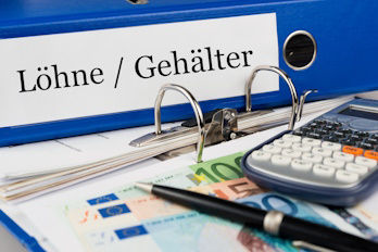 Ein Ordner Löhne / Gehälter liegt mit einem Taschenrechner, einem Stift und ein paar Geldscheinen auf einem Tisch