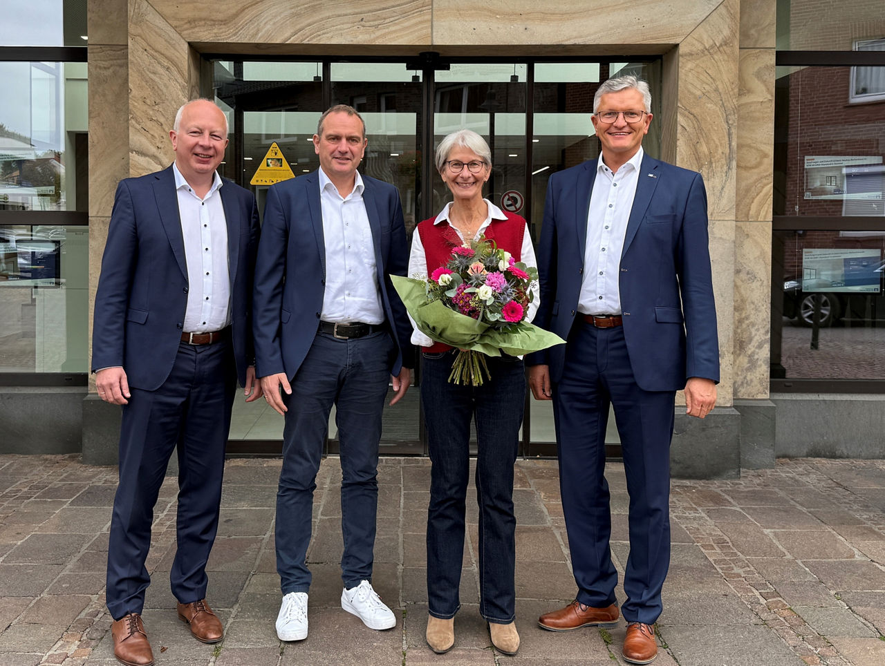 Drei Männer und eine Frauen haben sich zum Foto aufgestellt. Die Frau hat einen Blumenstrauß