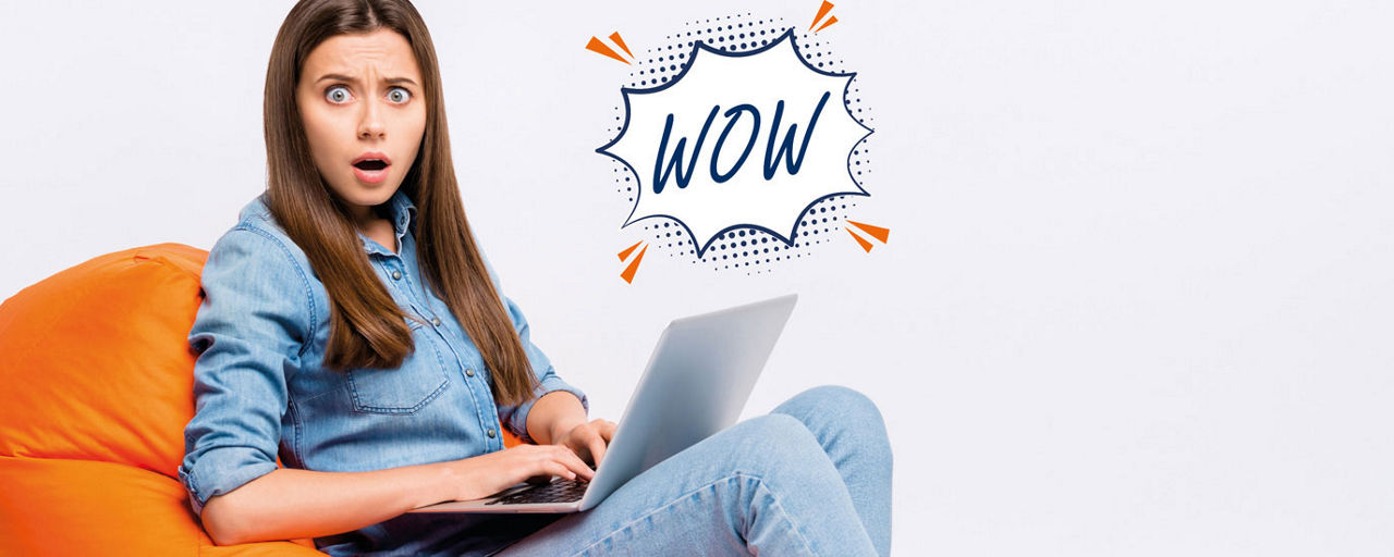 Erstaunte junge Frau auf dem Sofa mit einem Notebook