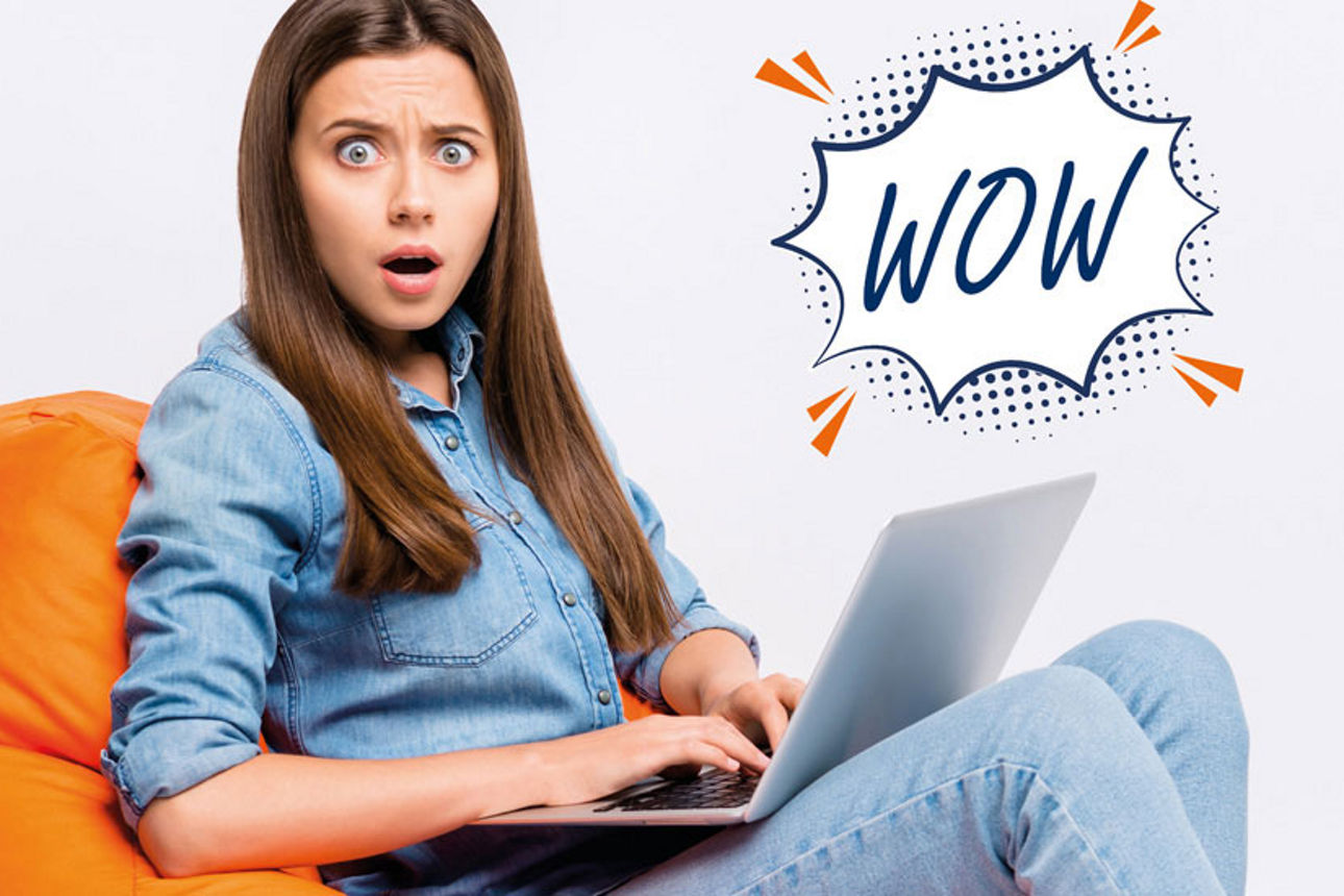 Erstaunte junge Frau auf dem Sofa mit einem Notebook