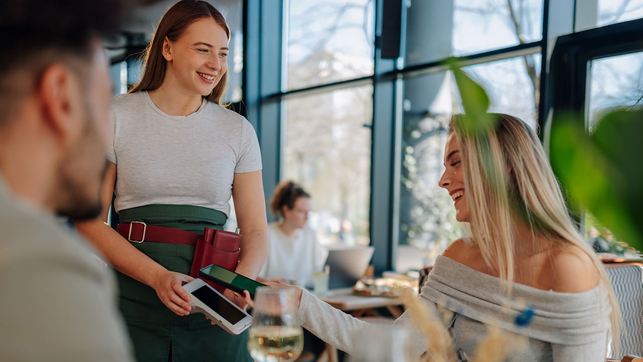Eine Frau bezahlt lachend mit ihrem Smartphone