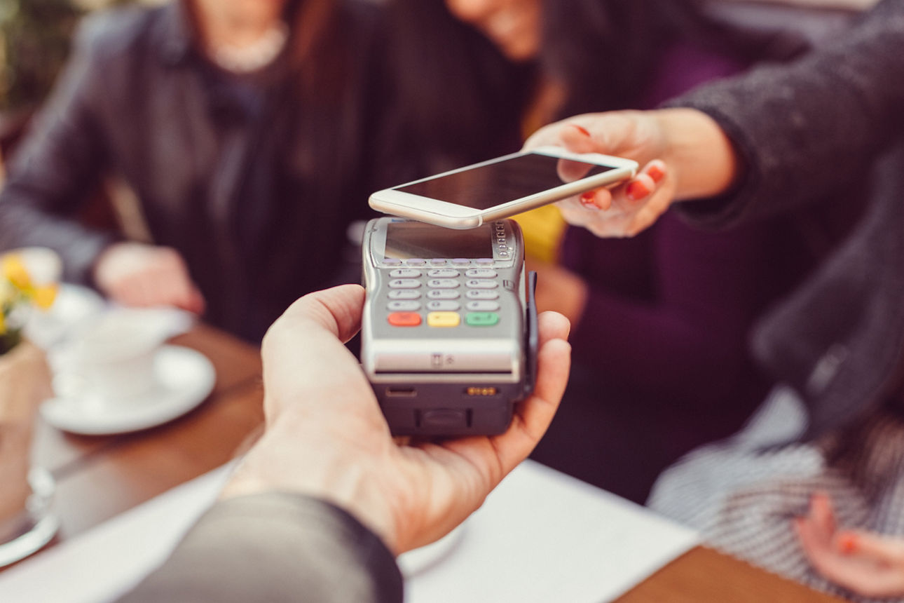 Eine Frau zahlt kontaktlos mit einem Smartphone an einem Zahlungsterminal