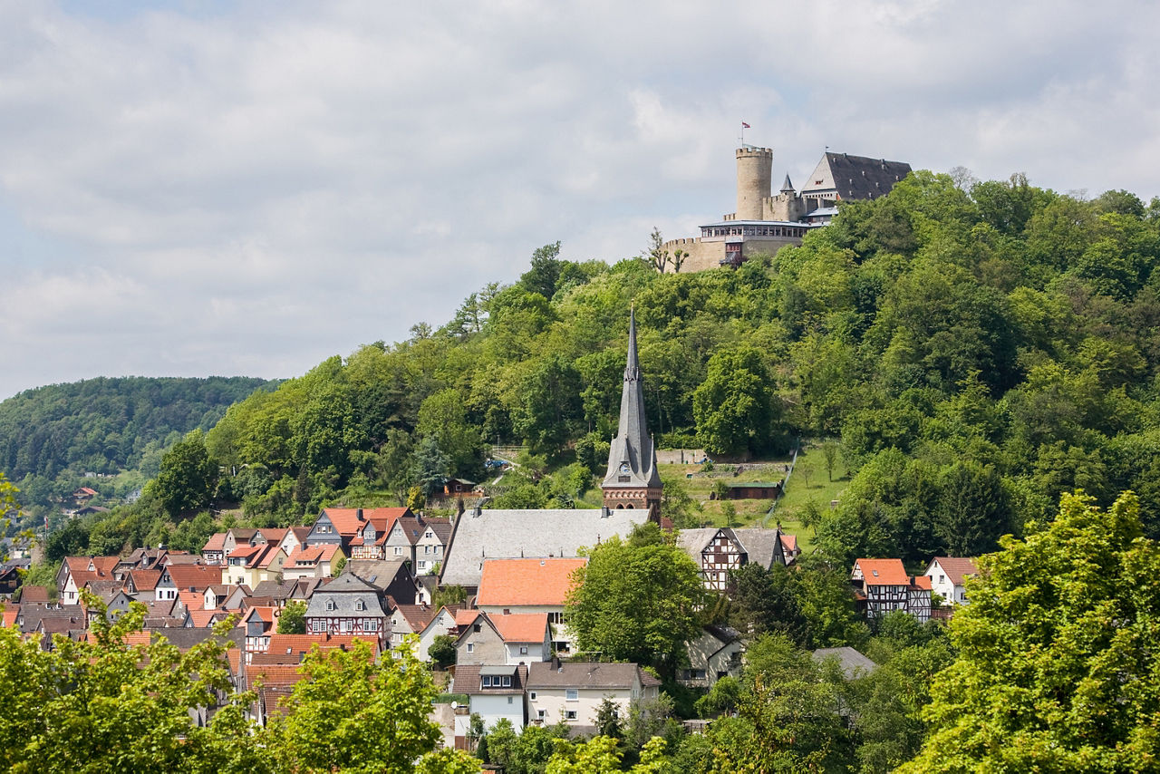Blick auf die Stadt Biedenkopf mit ihren Fachwerkhäusern am Hang und dem Schloss Biedenkopf, das auf einem bewaldeten Hügel thront.